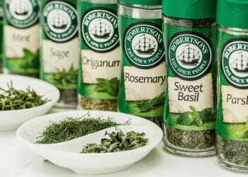 Assorted dried herbs in branded spice jars with bowls of loose herbs in the foreground.