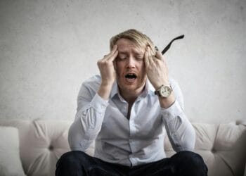 Stressed man sitting on couch, feeling overwhelmed and frustrated, expressing mental strain.