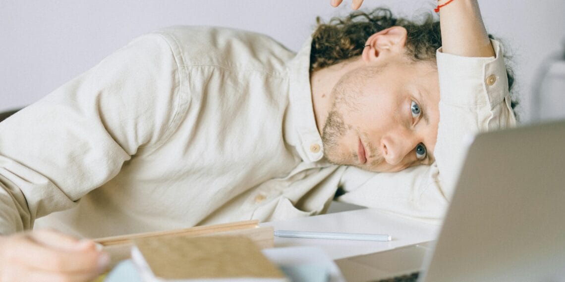 A tired Caucasian man at a desk, showing signs of exhaustion and stress, exemplifying workplace burnout.